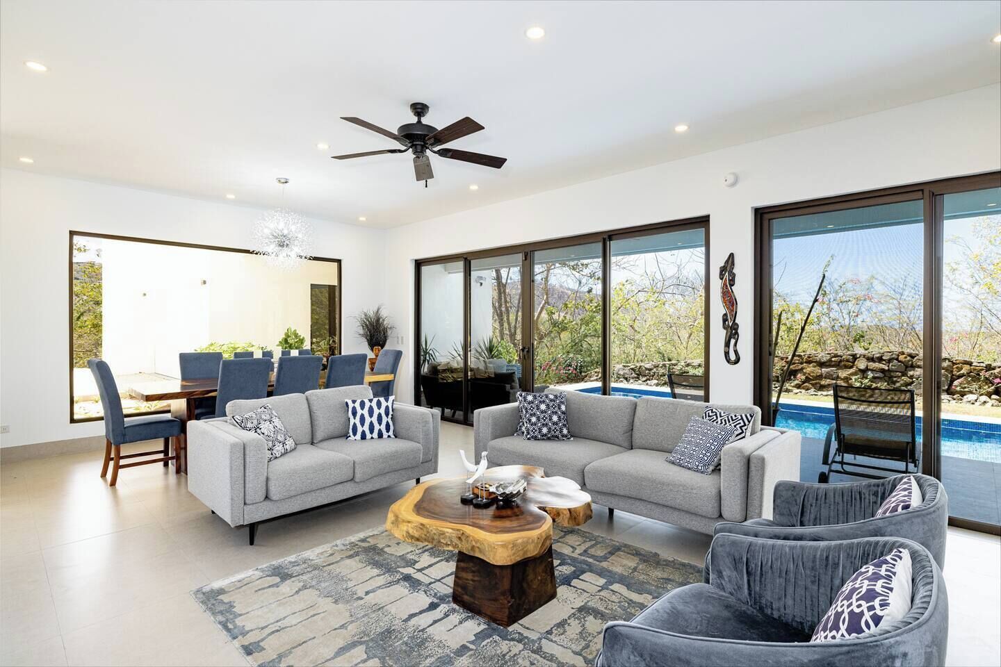 A modern living room with two grey sofas, a wooden coffee table, and a dining area with blue chairs and a glass table.