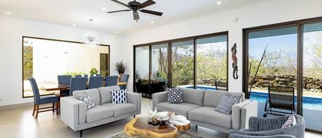 A modern living room with two grey sofas, a wooden coffee table, and a dining area with blue chairs and a glass table.