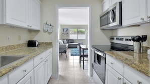 A modern kitchen with white cabinets, granite countertops, a microwave, and a stove. There is a dining area with a gray sofa and a blue rug. - Beautiful spacious 2bd, w/d, bbq, yard, pets allowed, free parking  (Delray Beach)