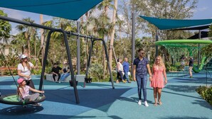 A playground with swings, a netted climbing area, and a seating area. - National Park Home Base Between Miami & The Keys (Homestead)