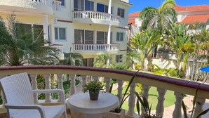 A balcony with white wicker furniture, a small round table, and potted plants. - Modern 2BR in Cabarete • Pool • Beach Walk (Cabarete)