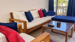 A room with a wooden sofa, a glass coffee table, and a matching armchair. - Modern 2BR in Cabarete • Pool • Beach Walk (Cabarete)