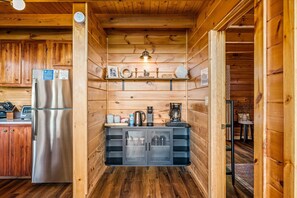 A compact kitchen with wooden walls, a stainless steel refrigerator, a coffee maker, and a built-in cabinet with shelves. - 4 King Suites & Jacuzzis | Decorated for Christmas | Hot Tub | Sleeps 12 (Sevierville)