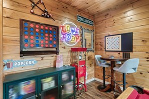 A room with a dartboard, a neon sign reading "GAME ROOM", a popcorn sign, a jukebox, and a jukebox with a neon sign.