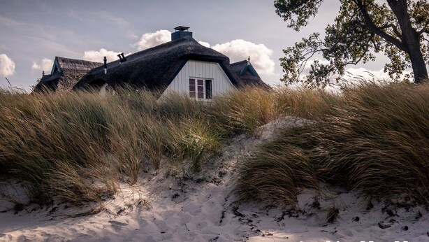 A thatched-roof house with a white window, surrounded by sand dunes and grass. - Apartment Famli Relax **** Villa Störtebeker in Göhren (Göhren)