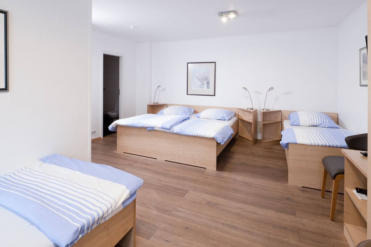 Habitación de hotel con dos camas, un escritorio y una silla. Hay un cuadro en la pared y una puerta que da al baño.