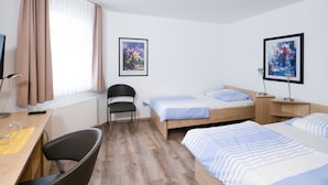 Une chambre d’hôtel comprenant un lit, un bureau, une chaise, une fenêtre avec des rideaux et deux tableaux encadrés accrochés au mur.