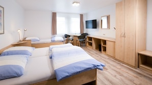 Une chambre d’hôtel avec deux lits, un bureau, une chaise, une télévision et une armoire.