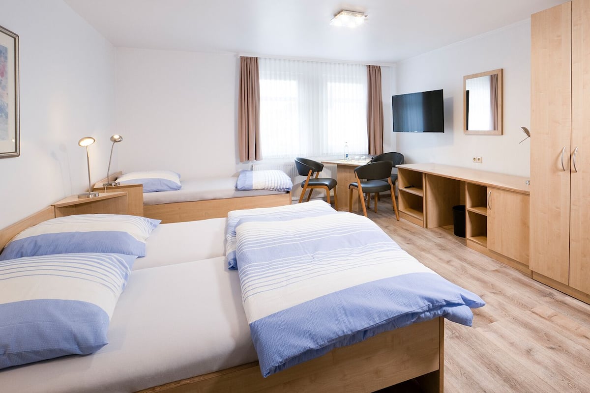 Habitación de hotel con dos camas, un escritorio, una silla, un televisor y un armario.