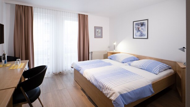 Une chambre d’hôtel avec un lit, un bureau, une chaise, une lampe et deux tableaux encadrés au mur.