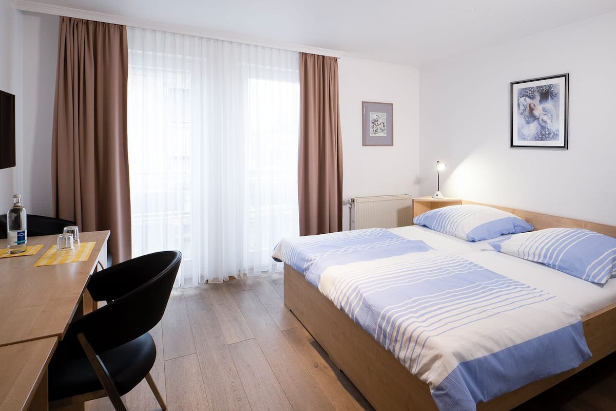 Una habitación de hotel con cama, escritorio, silla, lámpara y dos cuadros en la pared.