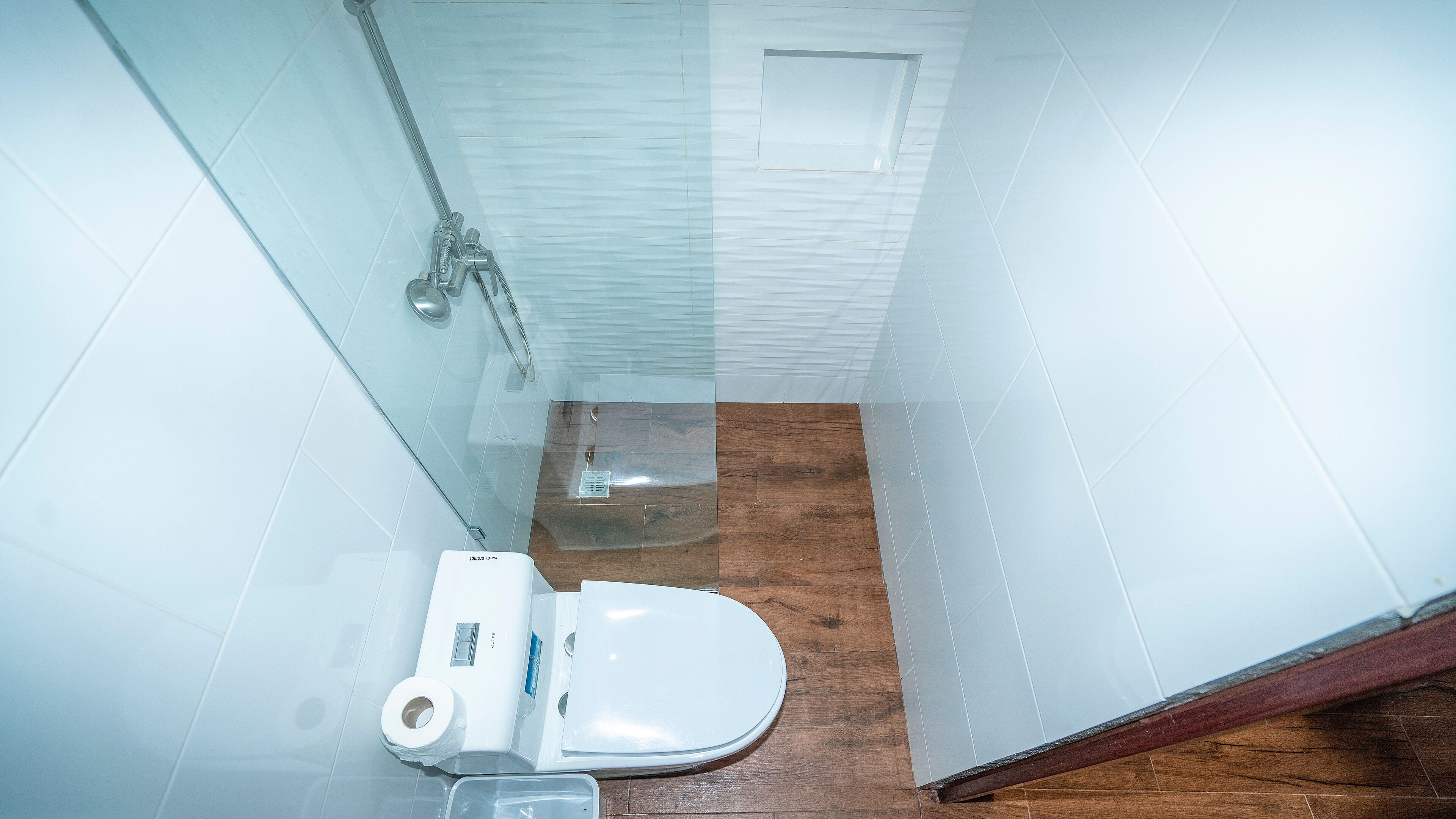 A bathroom with a white toilet, a shower, and a wooden floor.