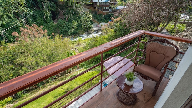 A balcony with a wooden railing, a wicker chair, and a small round table with a potted plant. - RIVER VIEW / VILLA FRENTE AL RIO / PEACE BY THE RIVER (Las Guázaras)