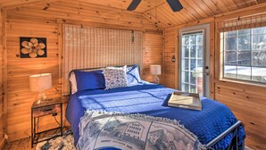 Un dormitorio de cabaña de madera con una cama, un ventilador de techo, una ventana y una puerta.