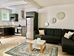 A modern living space with a kitchen, a black sofa, a coffee table, and decorative mirrors.