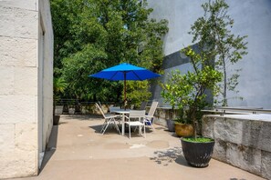 Una terrazza esterna con tavolo e sedie, un ombrello blu e piante in vaso.