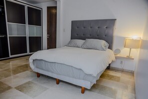 Un letto rifatto con un comodo poggiatesta grigio, una lampada da comodino e un'ampia armadio con ante scorrevoli.
