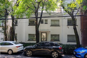 A building with multiple windows and a door, surrounded by trees and parked cars.
