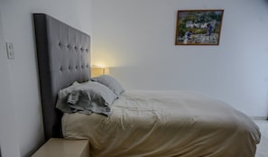 A bedroom with a tufted headboard, a bedside table, a lamp, and a framed picture on the wall.