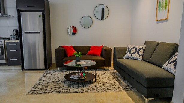 Uma sala de estar moderna com sofá, mesa de centro e área de cozinha com geladeira.