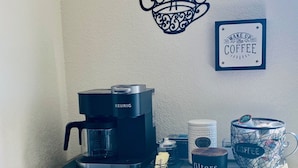 Un espai de cafè amb una màquina de cafè Keurig, una tassa de cafè i un quadre penjat a la paret.