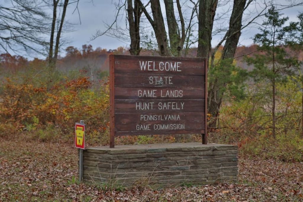 Uma placa de madeira com a inscrição Pennsylvania Game Lands, incluindo um lembrete de segurança.