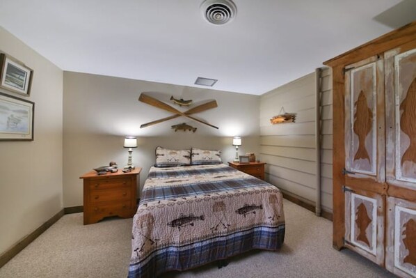 Un dormitorio con cama, dos mesitas de noche, un armario de madera y un ventilador de techo.