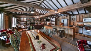 Un interior rústico con vigas de madera a la vista, una larga mesa de comedor con sillas, una zona de cocina y una barra.