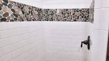 A shower with white tiled walls and a mosaic tile floor.