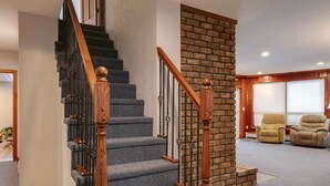 A staircase with wooden balusters and carpeted steps, leading to a room with a brick accent wall and two beige armchairs. - Kettle Creek Hills Lodge: Exceptional Views! (Elk Township)