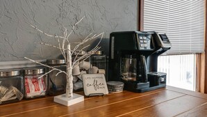 A coffee machine on a wooden counter with jars of coffee pods and a decorative branch. - Kettle Creek Hills Lodge: Exceptional Views! (Elk Township)