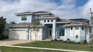 A two-story house with a garage, a small front yard, and a driveway. - Entire 4 Bedroom W/Pool Access (Marco Island)