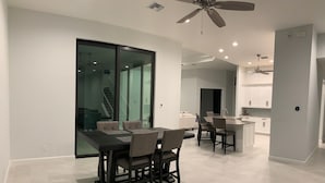 A modern kitchen with white cabinets, a central island, and a dining area with a dark table and chairs. - Entire 4 Bedroom W/Pool Access (Marco Island)