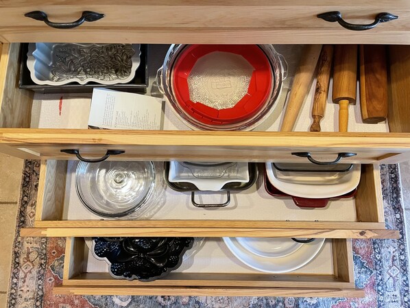 A drawer with various kitchen utensils and dishes, including a red bowl, a black bowl, and a white plate.