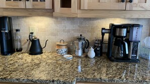 A kitchen with granite countertops, wooden cabinets, and various coffee-making equipment.