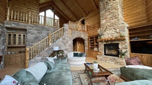 A spacious living room with a stone fireplace, a wooden staircase, and a cozy seating area.