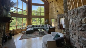 A spacious log cabin with large windows, a stone fireplace, and a cozy seating area.