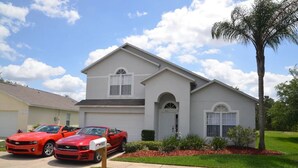 Una casa a due piani con un garage, un vialetto e due auto sportive rosse parcheggiate davanti.