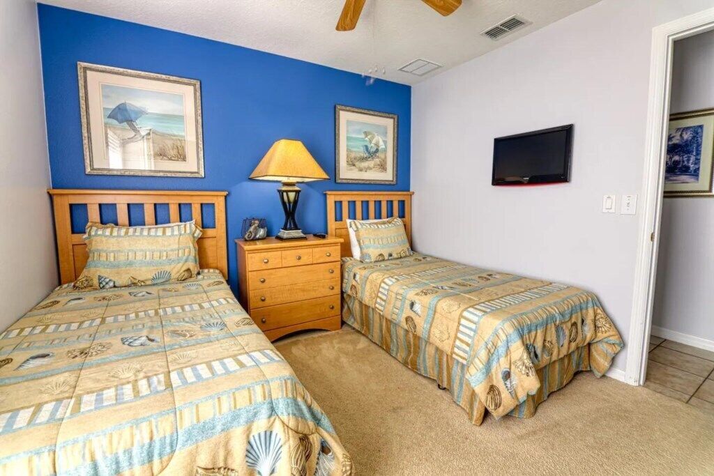 A bedroom with two beds, a nightstand, a lamp, and a TV.