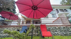 Ein Gebäude mit mehreren roten Sonnenschirmen, einer Steinmauer und zwei Liegestühlen.