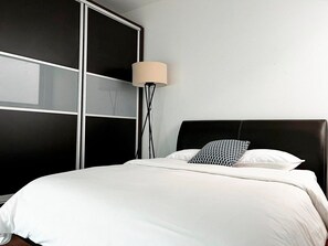 Un lit avec une literie blanche, une tête de lit noire et une lampe de sol avec un abat-jour beige.