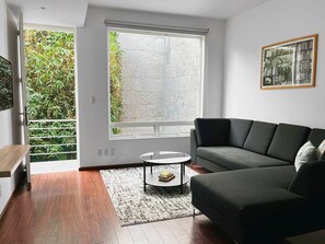 A modern living room with a dark sofa, a round coffee table, and a large window with a view of greenery.