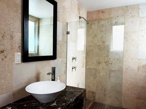 Une salle de bain avec un lavabo blanc, une cabine de douche en verre et un comptoir en marbre.