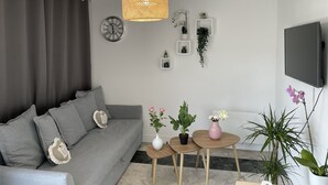 Ein modernes Wohnzimmer mit grauem Sofa, einem Wand-Fernseher und mehreren Blumentöpfen.