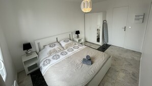 Ein Schlafzimmer mit Bett, Nachttischen, einer Pendelleuchte, einem Kleiderschrank und einem Spiegel.