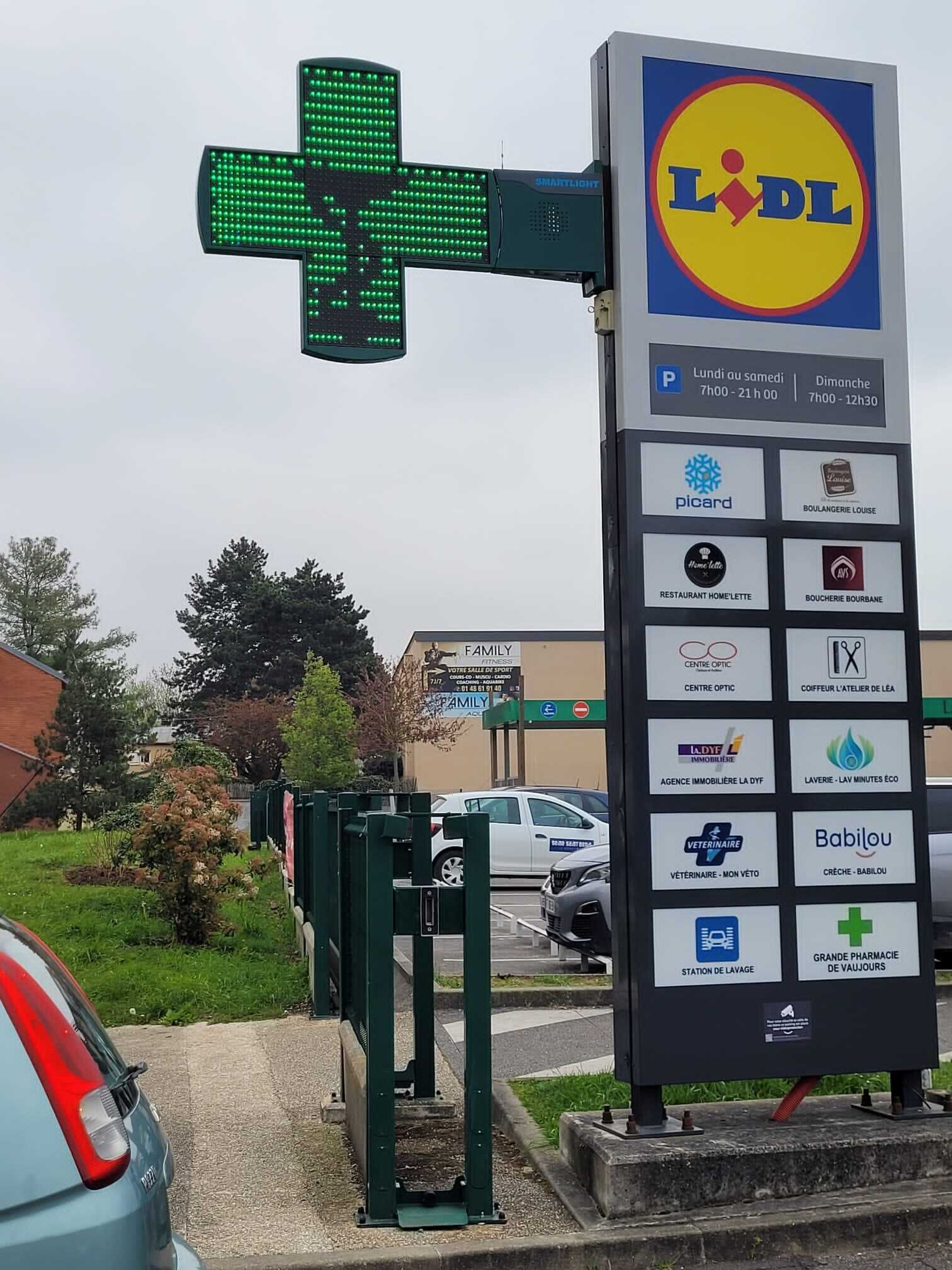 A Lidl store with a green cross sign, a parking sign, and a directory of local businesses including a gym, restaurant, and pharmacy.