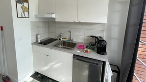 Eine kleine Küche mit weißen Schränken, einer Edelstahl-Spüle, einem Geschirrspüler und einer Kaffeemaschine.