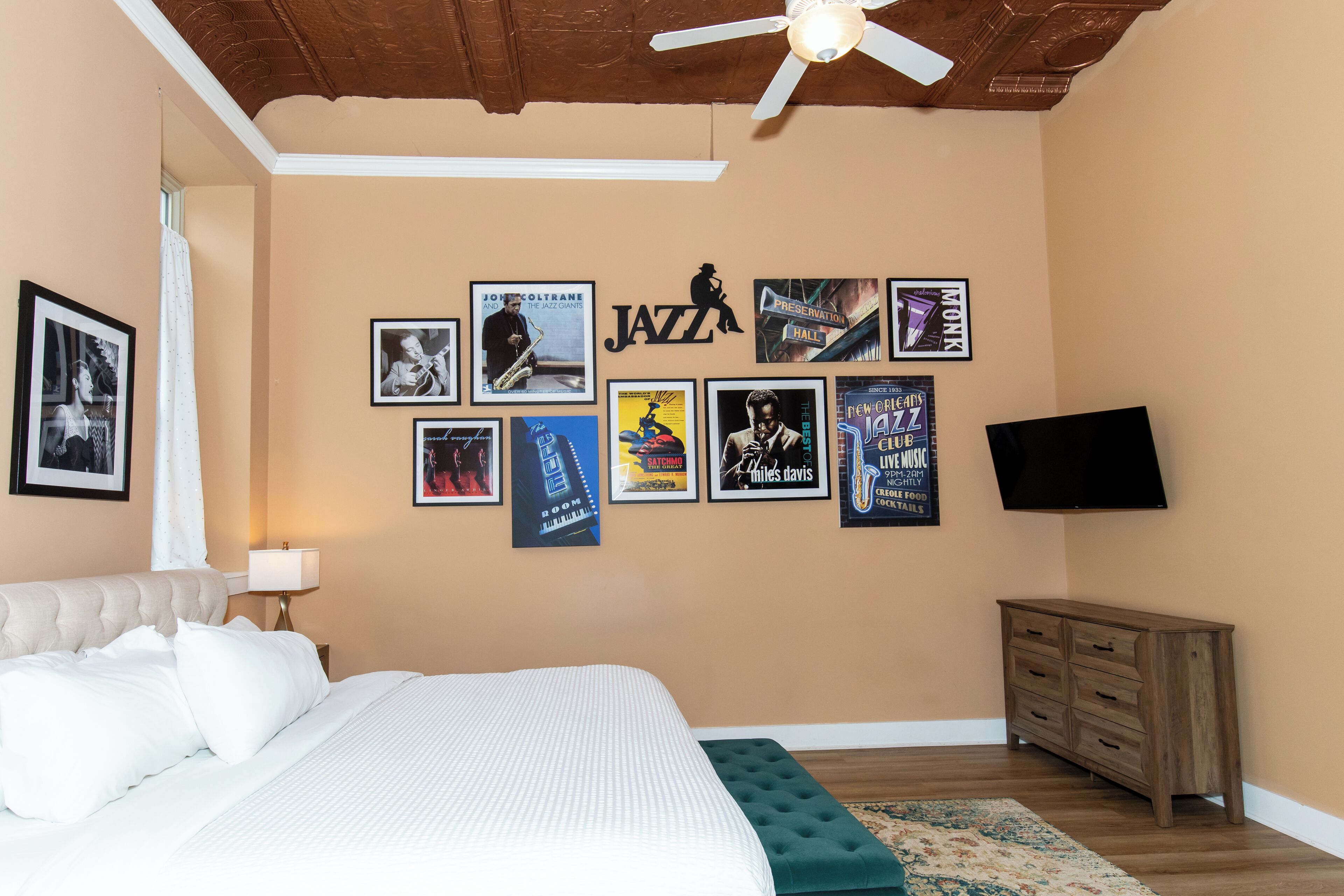 Une chambre à coucher avec un lit, un téléviseur fixé au mur et une série d’affiches encadrées accrochées au mur.