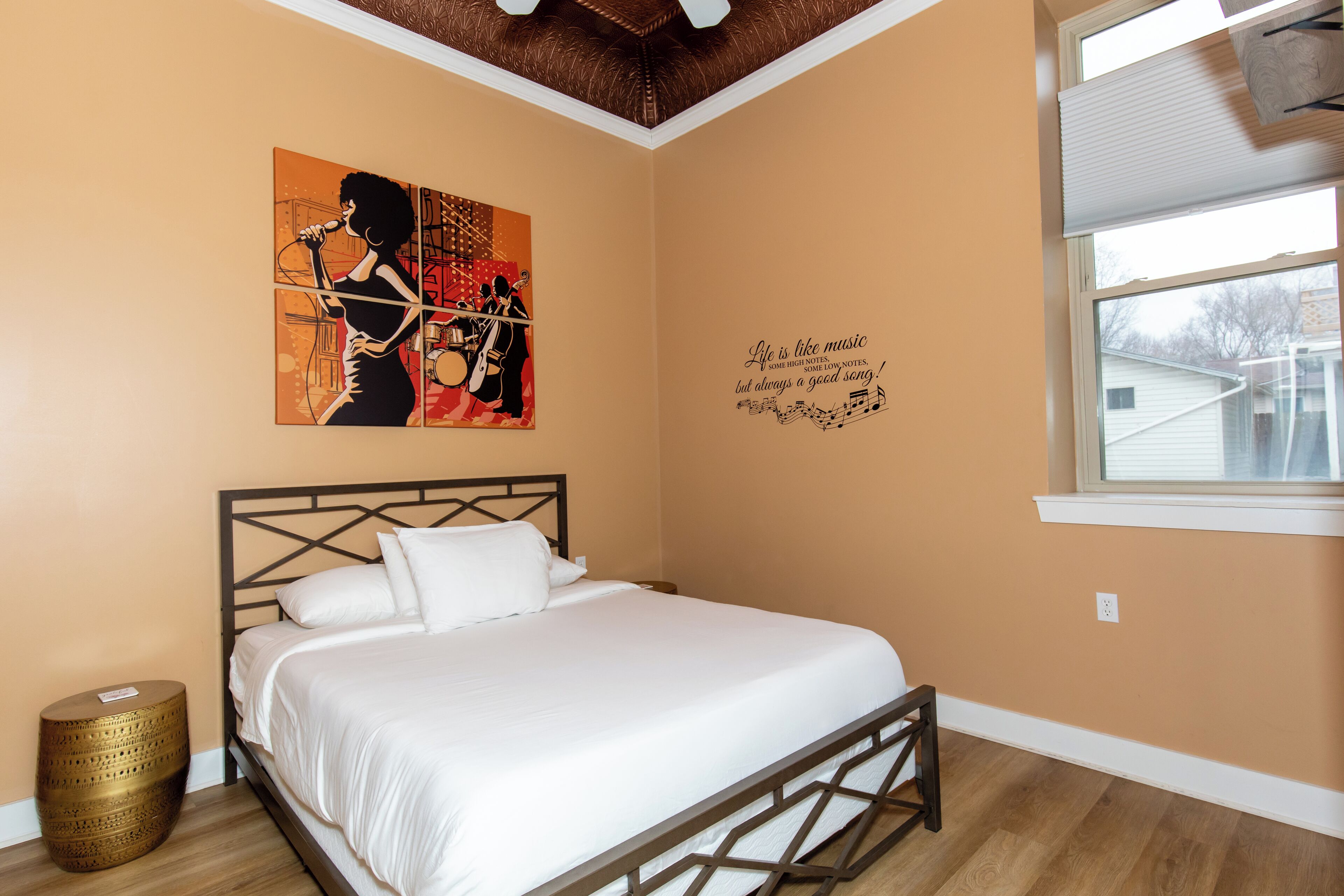 Un dormitorio con cama, una obra de arte en la pared, una frase decorativa y una ventana con persianas.