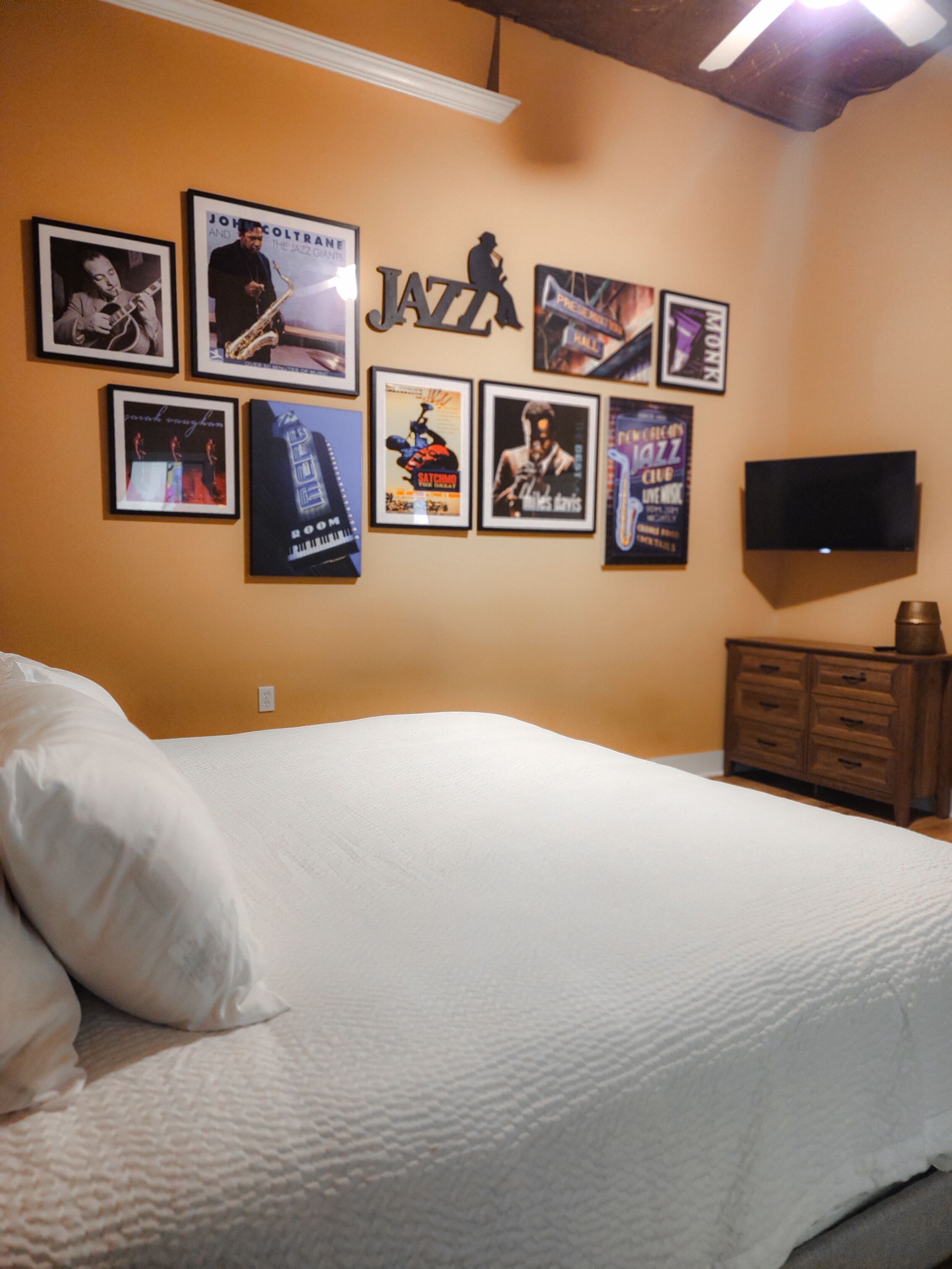 A bedroom with a bed, a dresser, a TV, and framed posters on the wall.